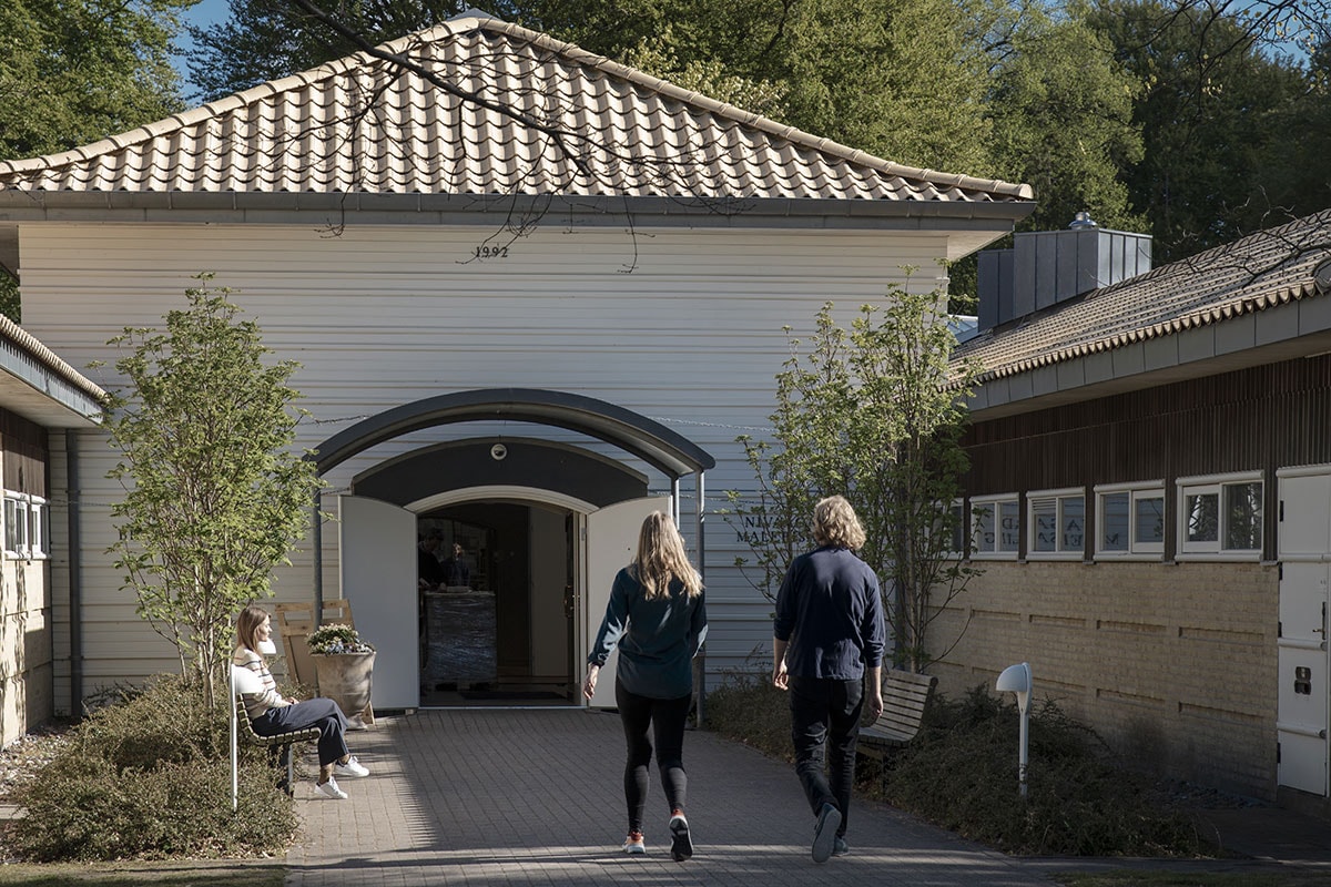 Två personer går med ryggen mot en vit byggnad.