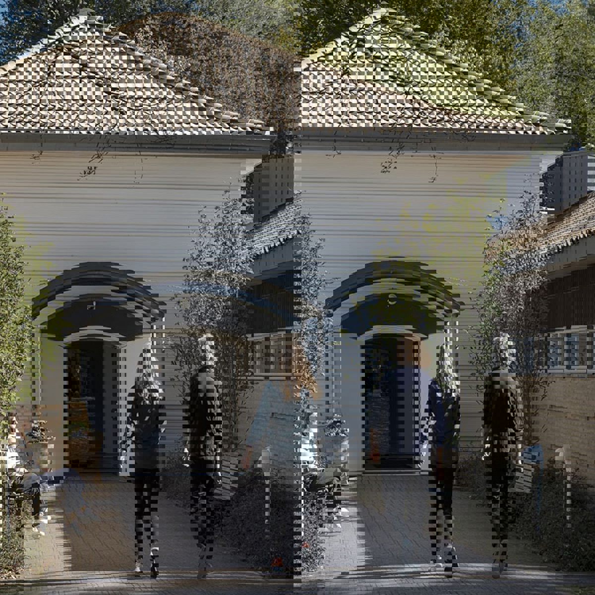 Två personer går med ryggen mot en vit byggnad.