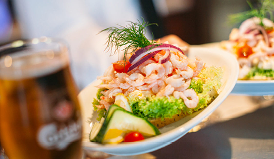 Rejemad på hvid tallerken med frisk salat, skiver af rødløg, citron og dild i en serveringssituation.