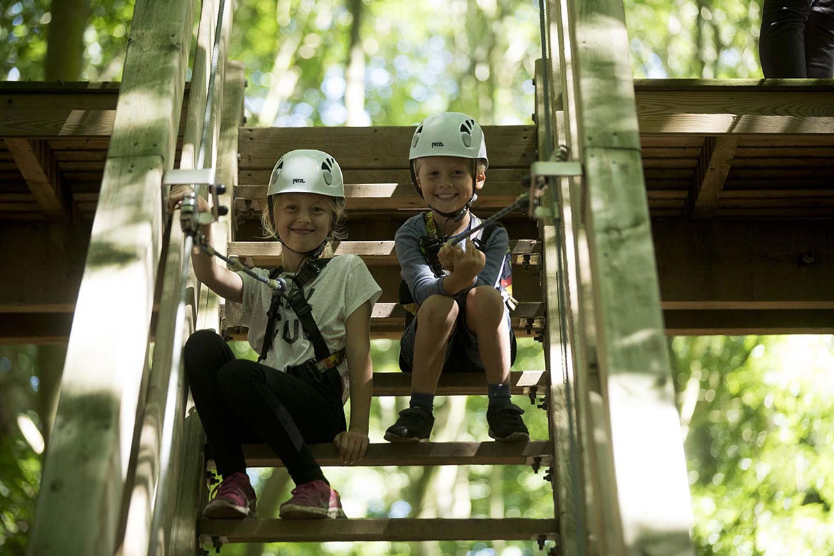 Två barn med säkerhetsutrustning sitter på en trappa i skogen.