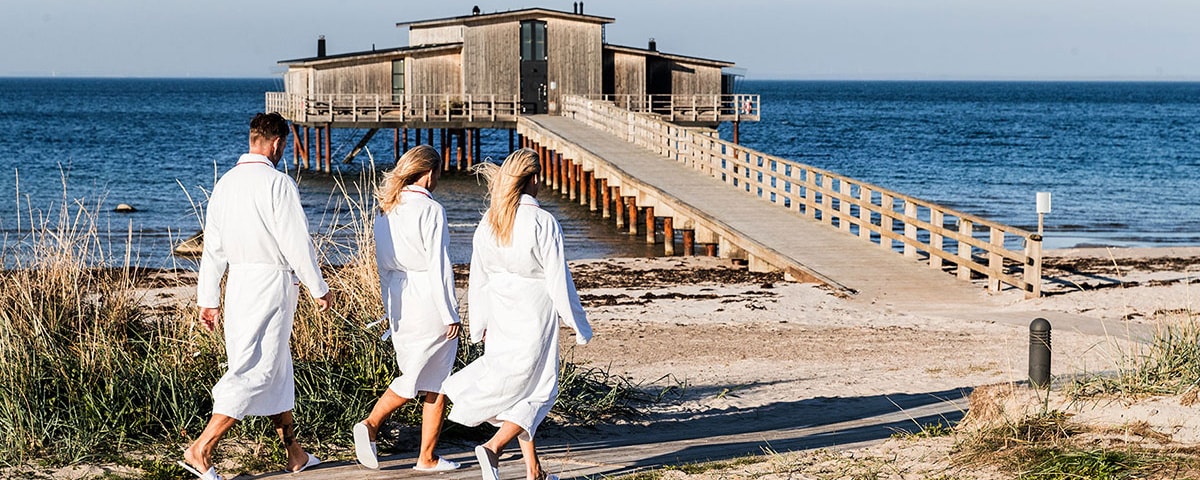 To blone kvinder i morgenkåber ses gående ud mod badebroen ved Hotel Skansen.