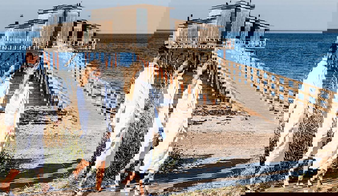 To blone kvinder i morgenkåber ses gående ud mod badebroen ved Hotel Skansen.