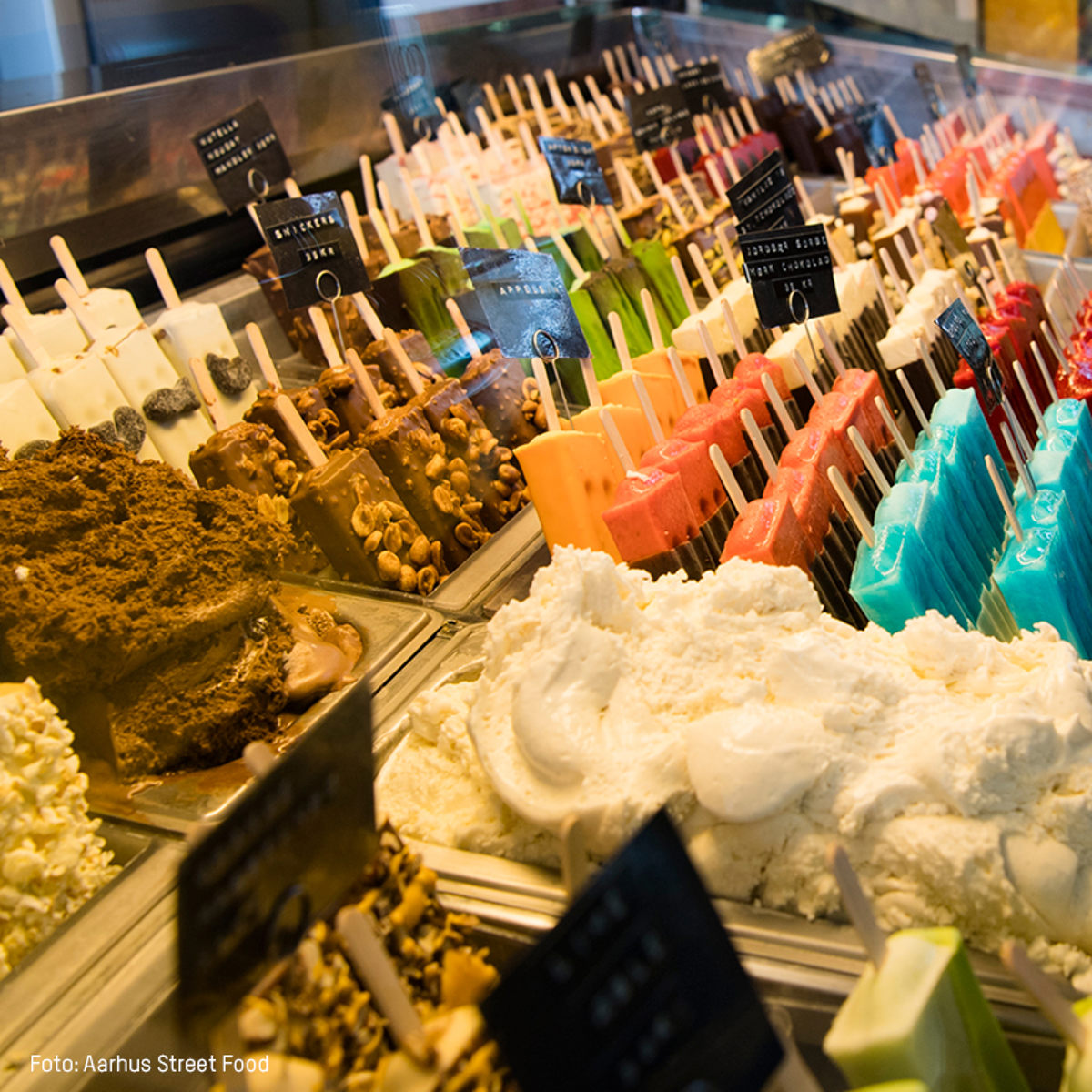 Diverse udvalg af farverige ispinde og is arrangeret i en køledisk hos Aarhus Street Food.