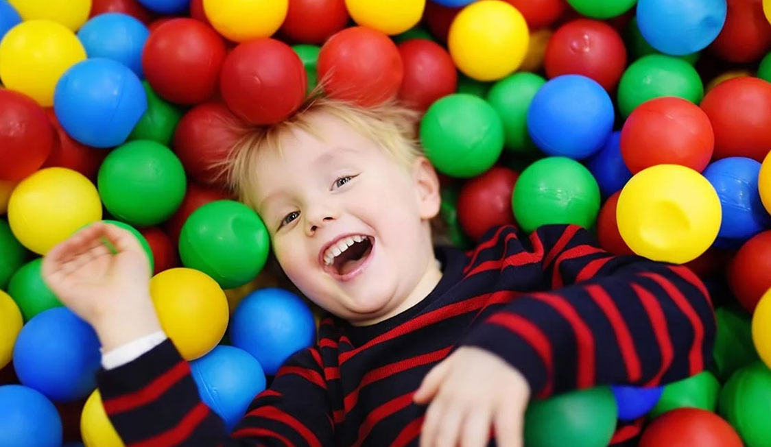 Lille barn i stribet trøje smiler i et hav af farverige plastikbolde.