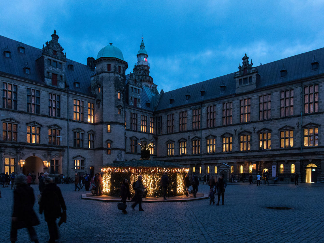 Gårdsplads med julelys og folk i skumringen ved Kronborg slot i Danmark.