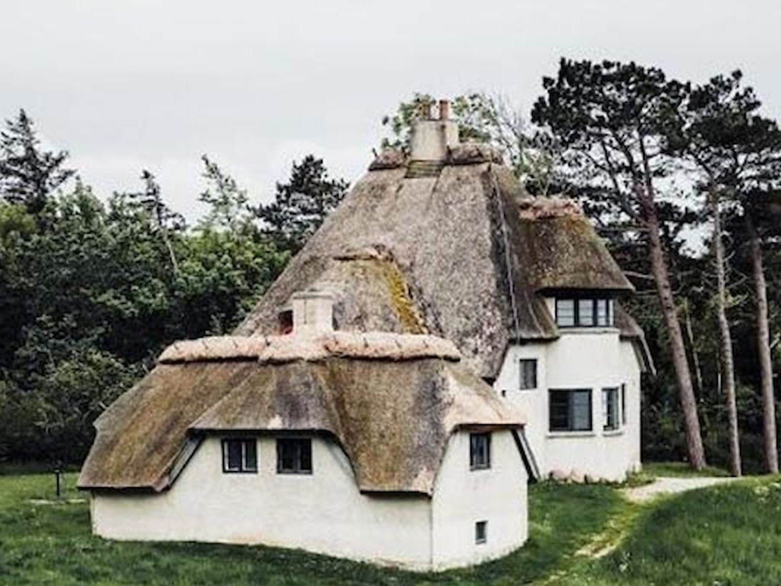Traditionellt stråtakshus känt som Knud Rasmussens Hus beläget i en grönskande miljö med skog i bakgrunden.