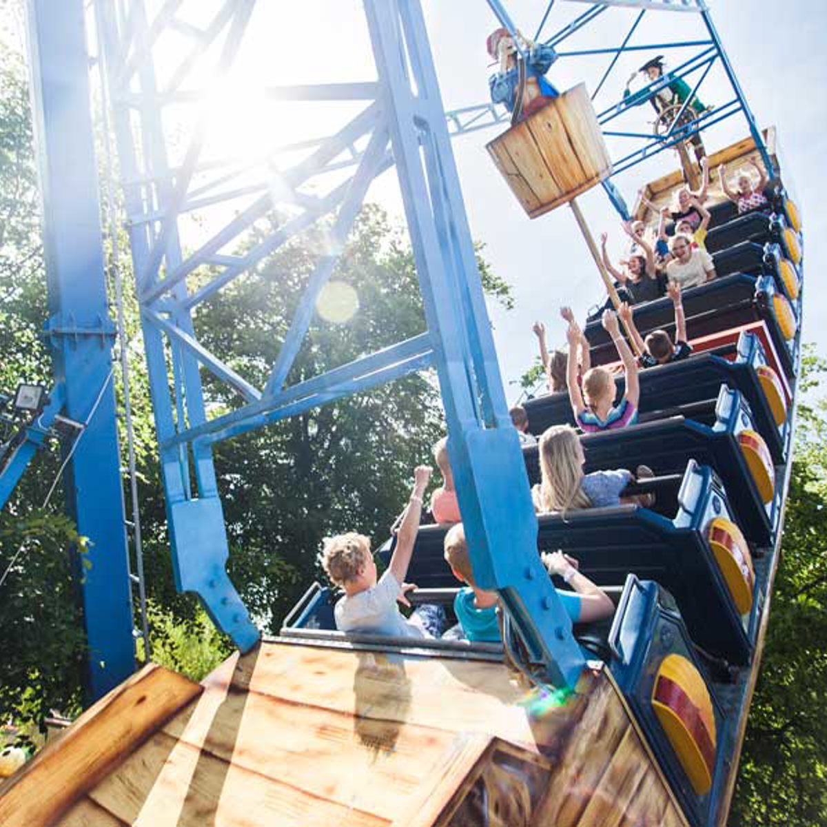 Børn nyder en tur på en farverig forlystelsessving i en forlystelsespark under en klar blå himmel.