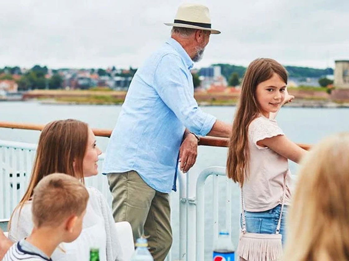 Familie nyder udsigten fra færgen over vandet, mens de sejler mod land i hyggelig samtale på dækket.