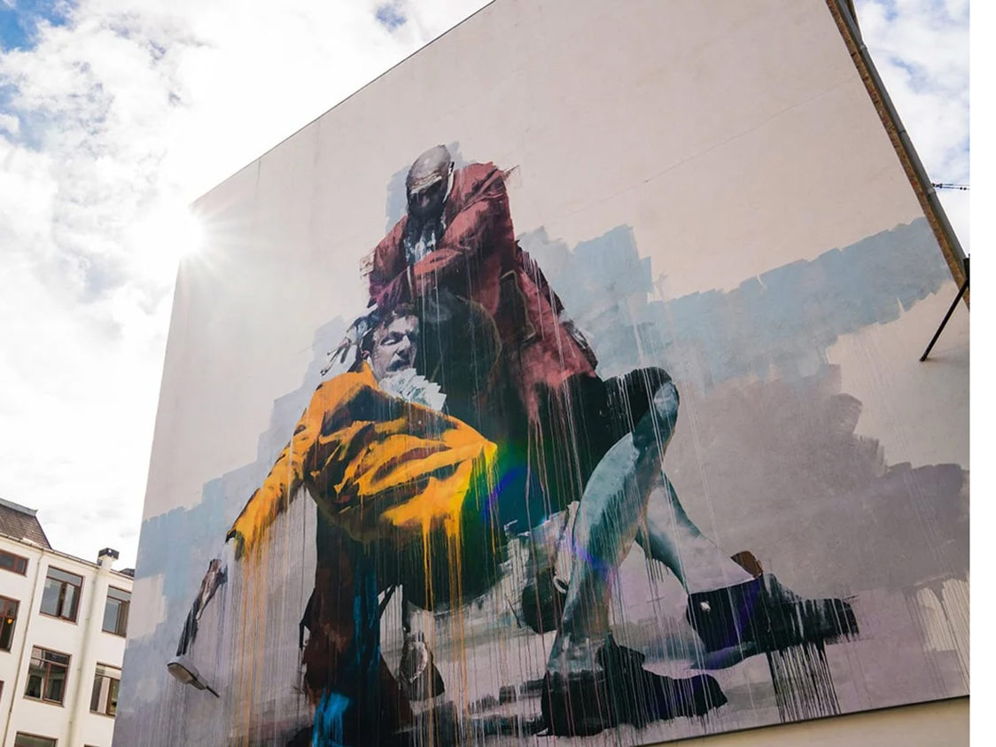 Väggmålning av två personer i färgglada kläder på en byggnad i Vesterbro under solens strålar.