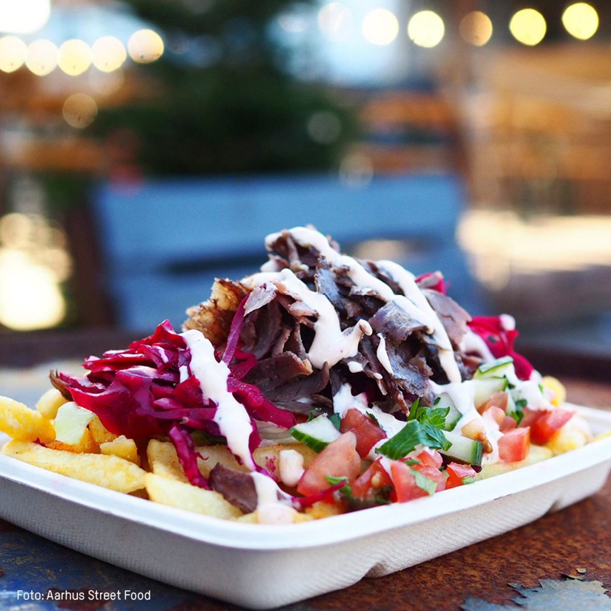 Stegte kartoffelbåde med ristede oksekødsstrimler, rødkål og grøntsager toppet med dressing i papbakke.