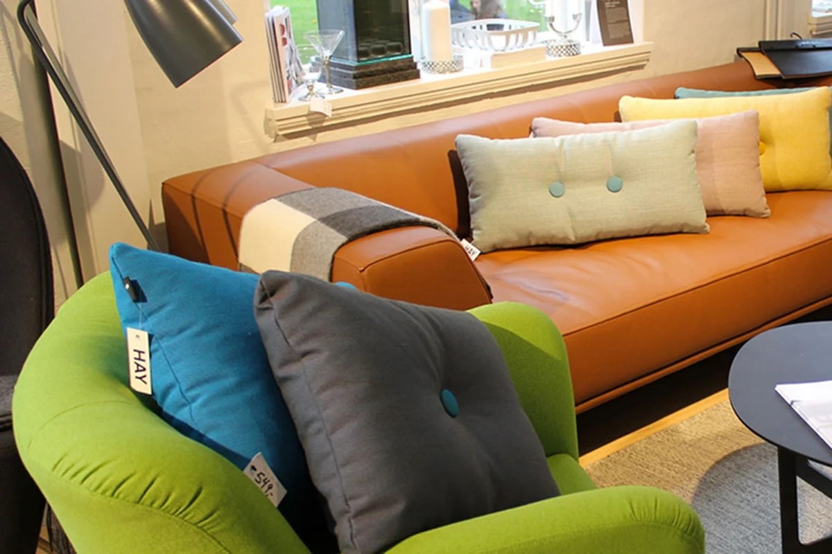 Brun skinnsoffa Olai med pastellfärgade kuddar och grön fåtölj i ett modernt vardagsrum.