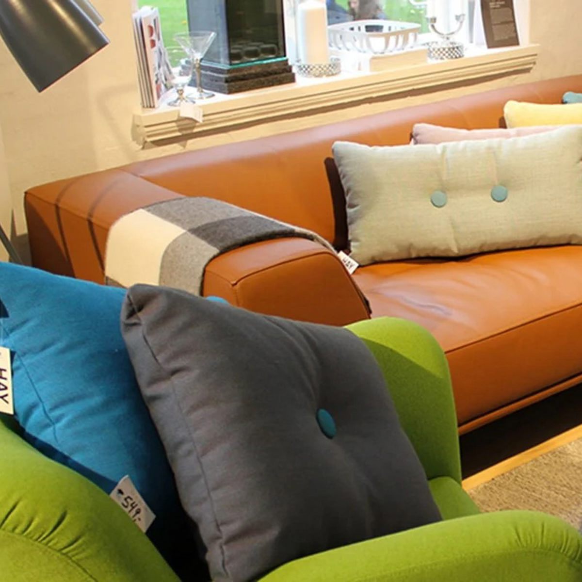 Brun skinnsoffa Olai med pastellfärgade kuddar och grön fåtölj i ett modernt vardagsrum.