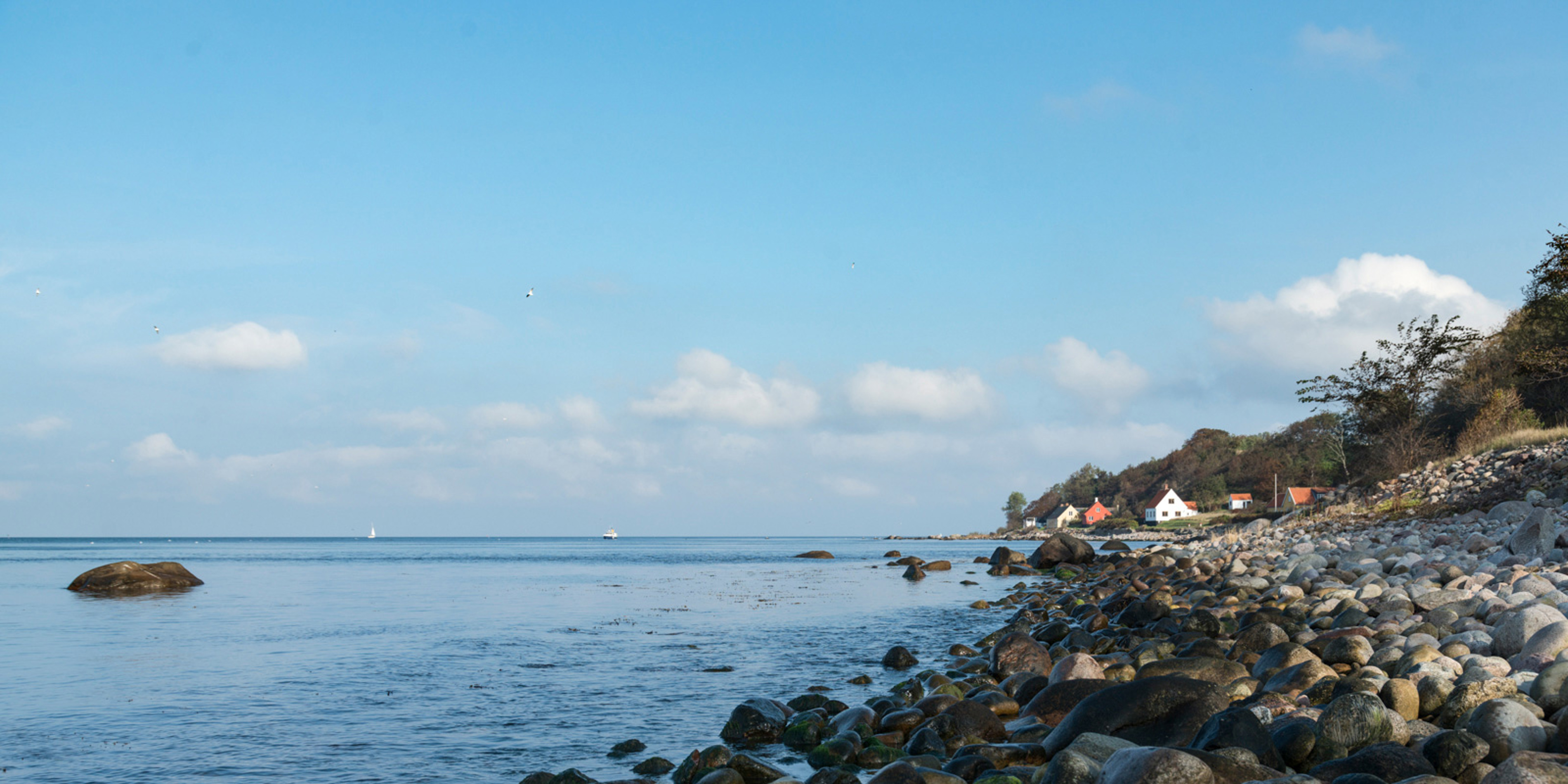 Küstenlinie mit Steinen trifft auf das Meer unter blauem Himmel.