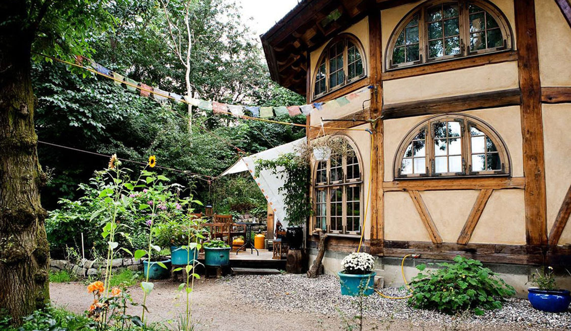 Charmigt halmtakstuga i grön trädgård med färgglada blomkrukor och hängande dekorationer.