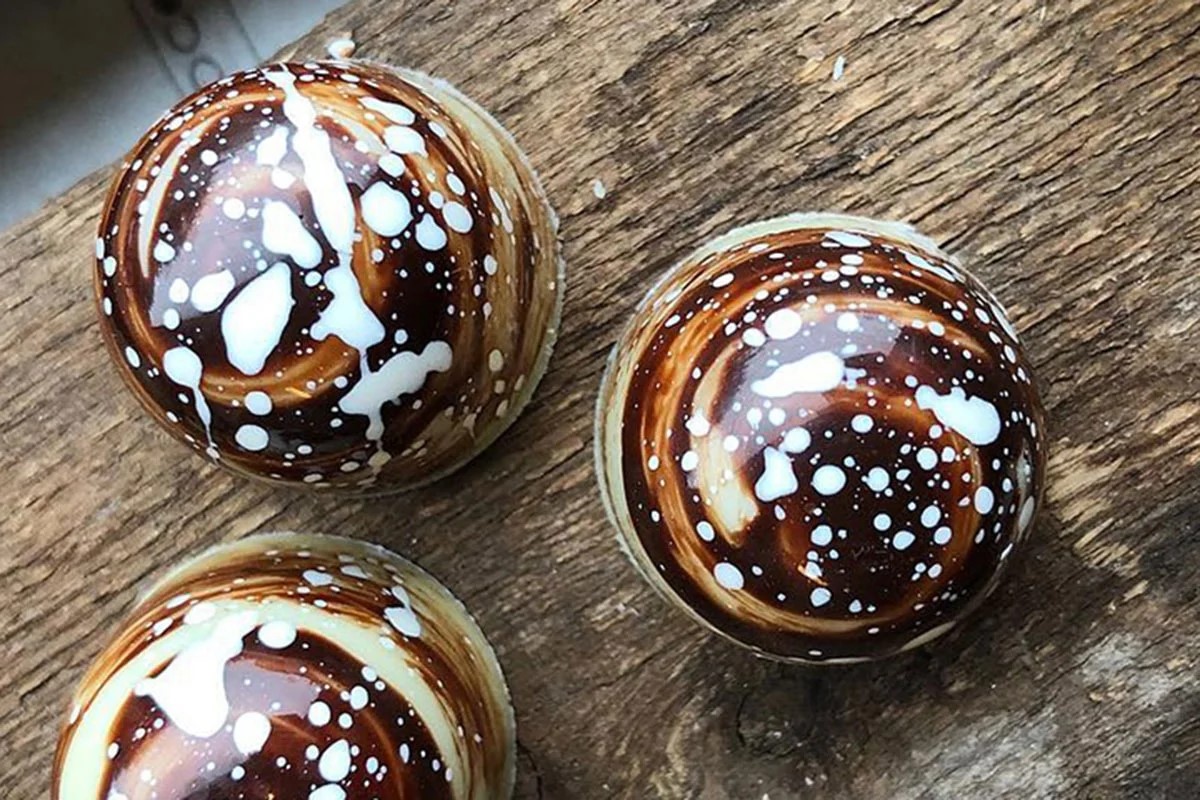 Chokoladekugler med kunstnerisk hvid og brun glasur på træbord, set oppefra.