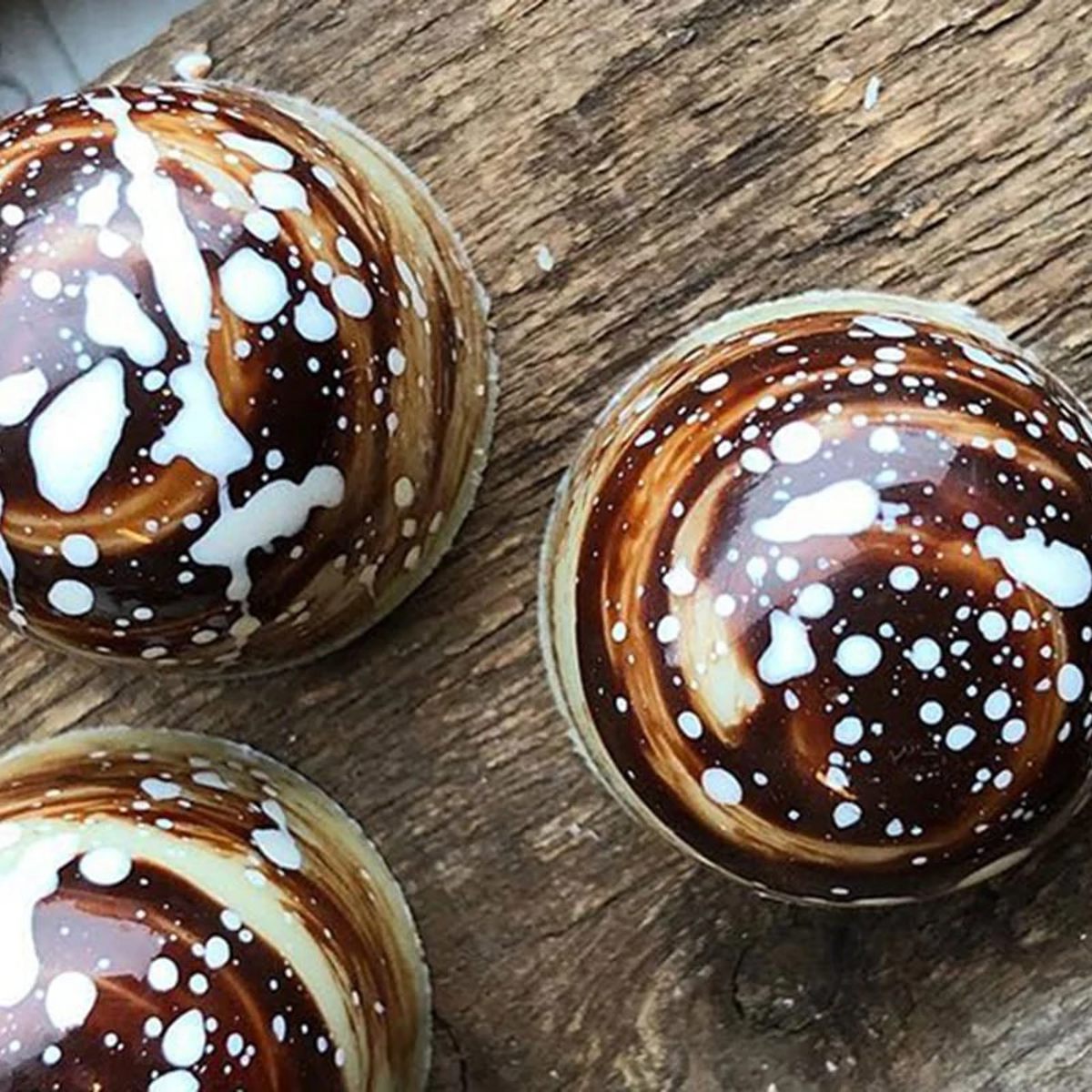 Chokoladekugler med kunstnerisk hvid og brun glasur på træbord, set oppefra.