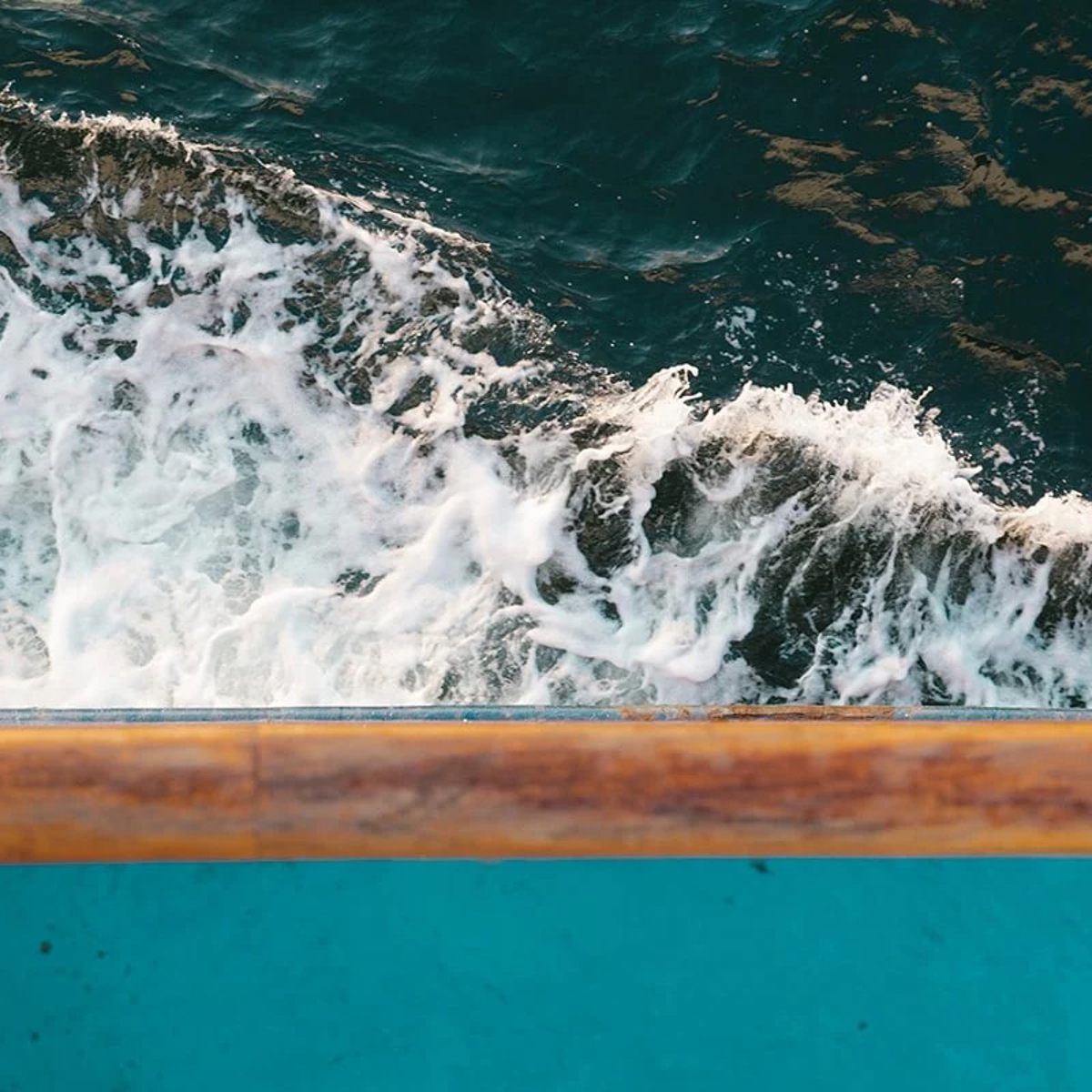 Aerial view of a ferry sailing through waves on open sea with focus on sea spray at boat's edge.