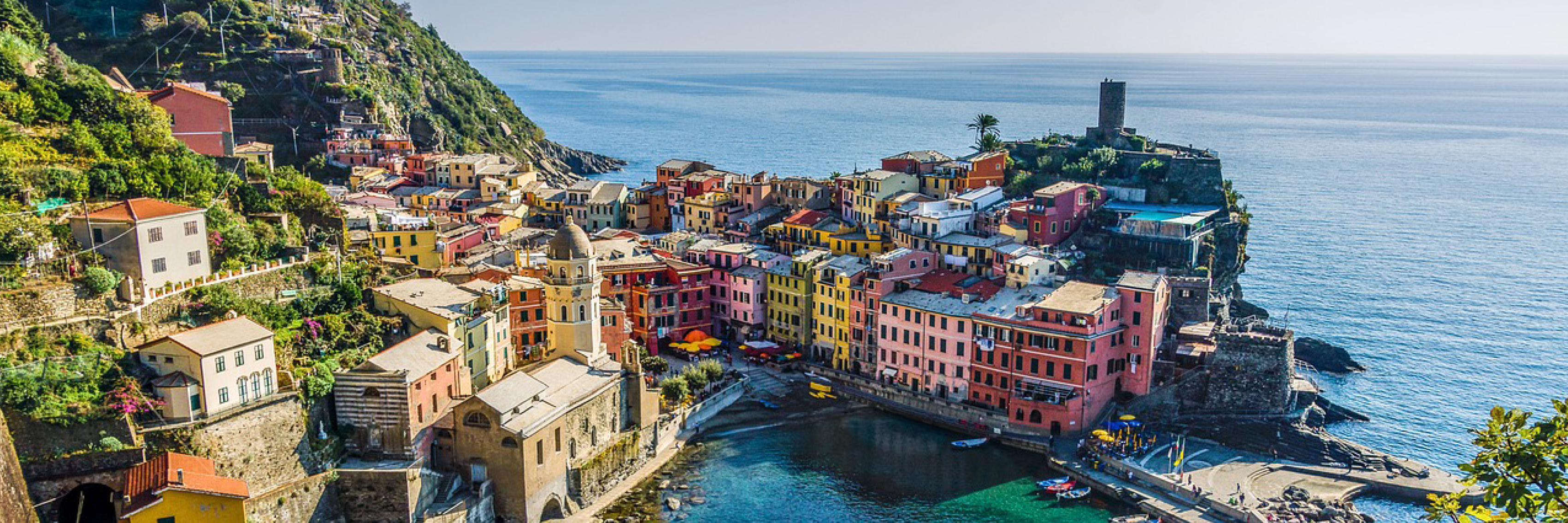Färgglada hus i en pittoresk Medelhavsstad vid klippig kustlinje och klarblått hav.