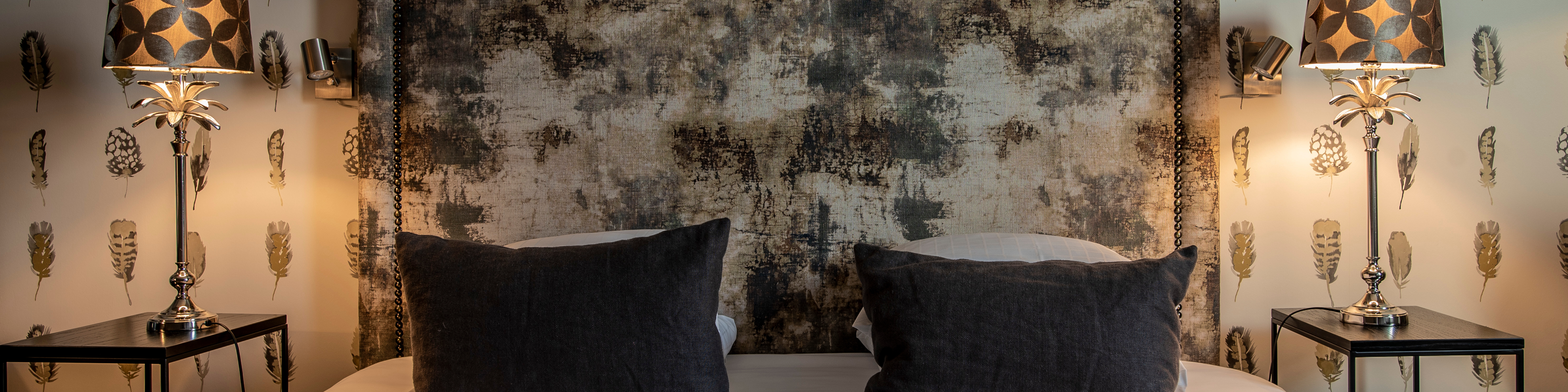 Moderne soveværelse med to mørkegrå puder på sengen og elegante lamper på natborde ved siden af.