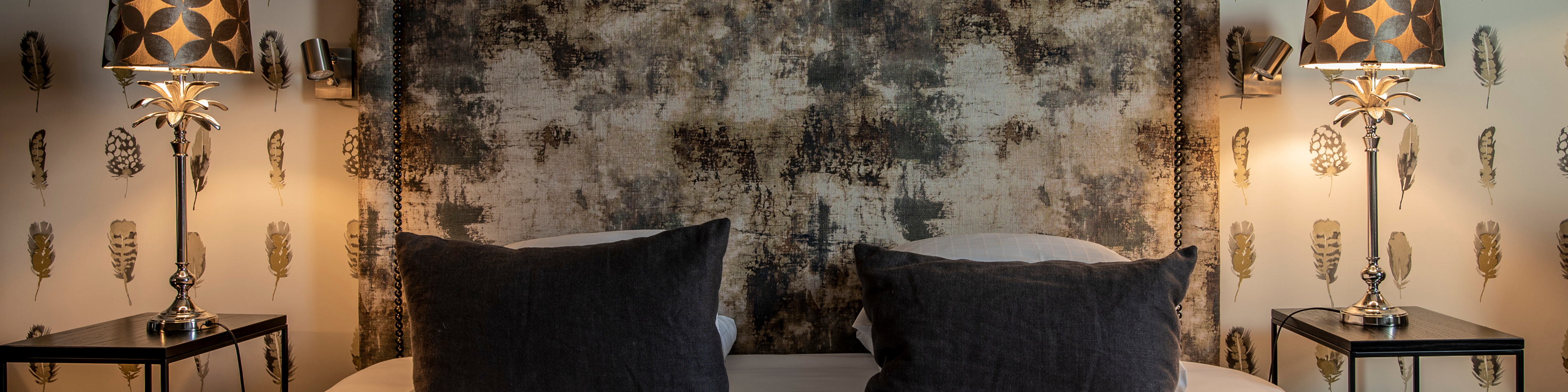 Moderne soveværelse med to mørkegrå puder på sengen og elegante lamper på natborde ved siden af.