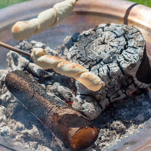 Esrum Lekplats pinnbröd rostas över glödande ved i en eldstad, perfekt för utomhusaktiviteter och friluftsliv.