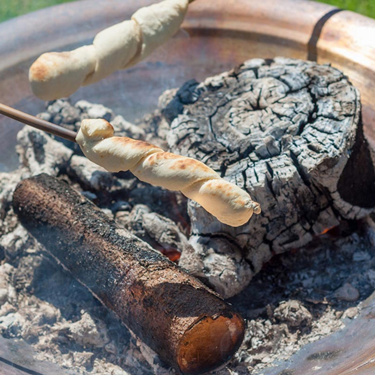 Esrum Lekplats pinnbröd rostas över glödande ved i en eldstad, perfekt för utomhusaktiviteter och friluftsliv.