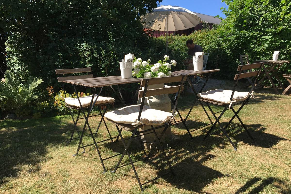 Caféborde med hynder står på en græsplæne med træer i baggrunden.