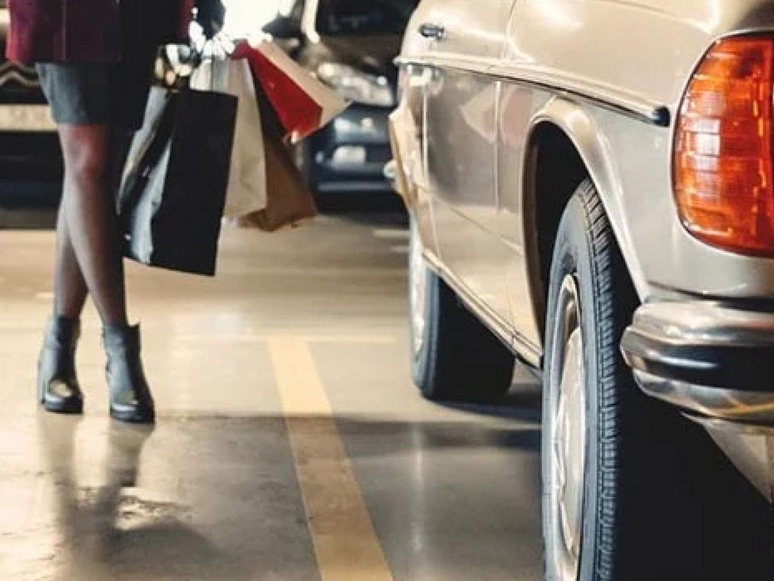 Kvinna bär shoppingkassar vid beige bil i parkeringsgarage.