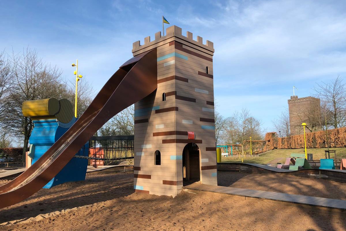 Karnan legeplads i sollys med gynger og rutsjebaner, set fra en høj vinkel.