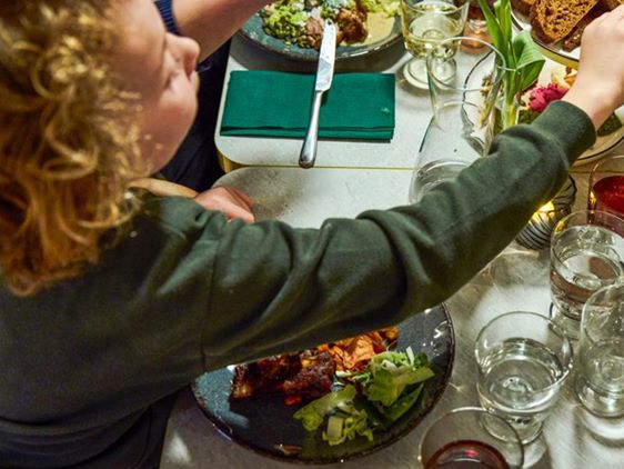 En person ved bordet tager mad fra en tallerken med ribs, salat og grøntsager.