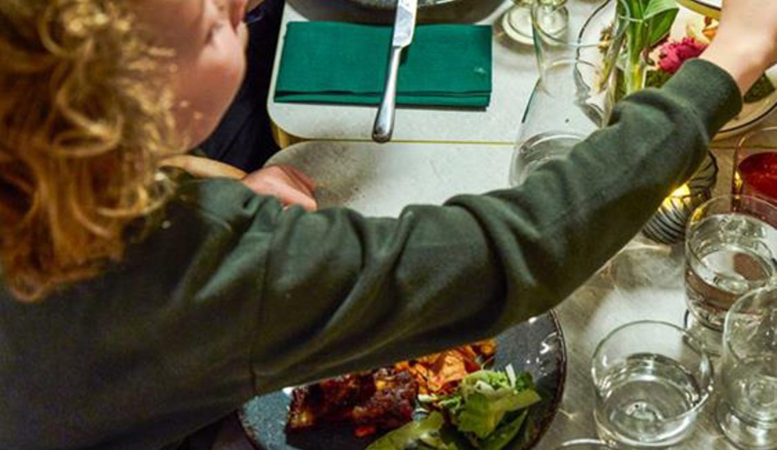 En person ved bordet tager mad fra en tallerken med ribs, salat og grøntsager.