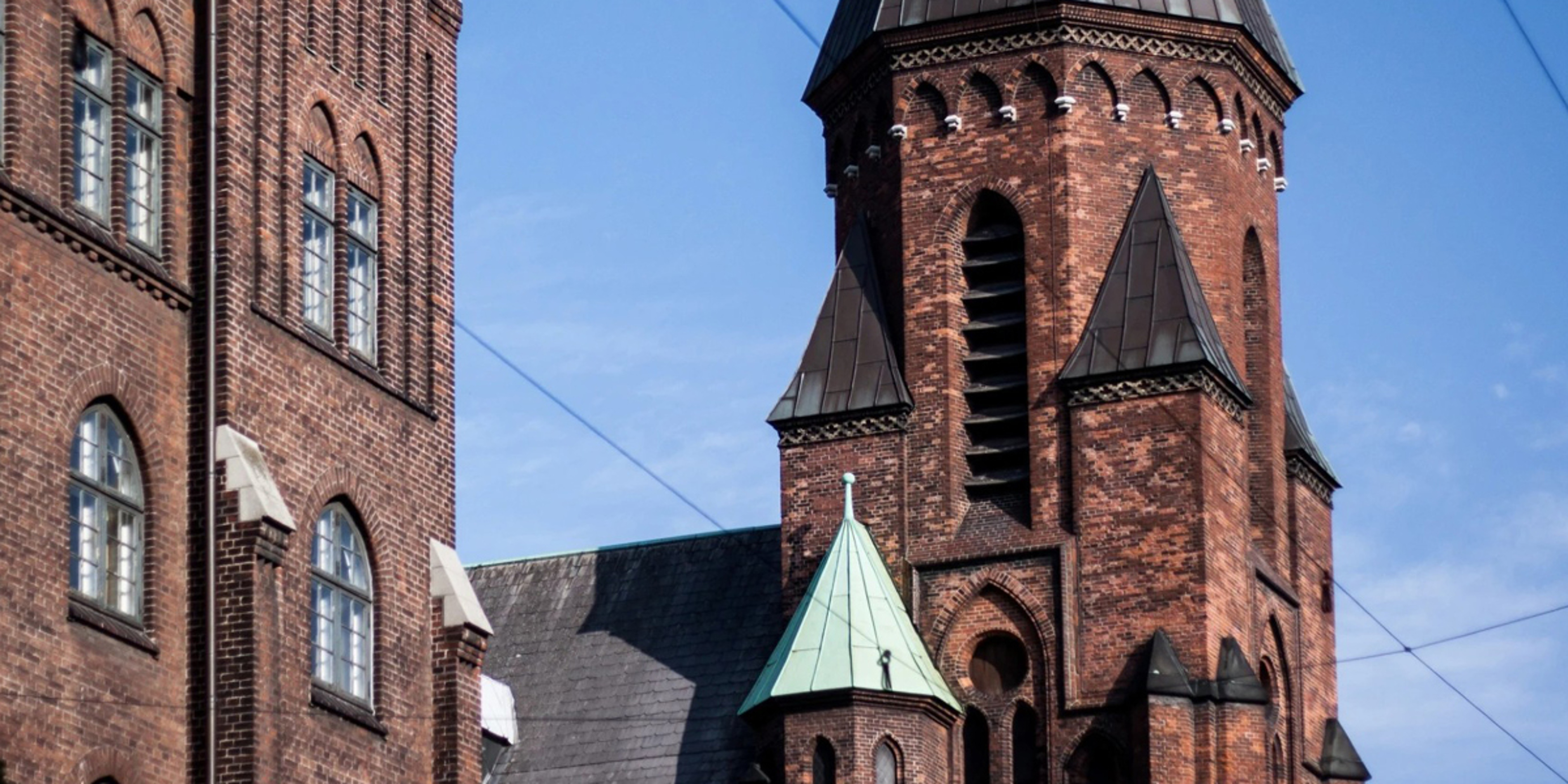 Rødstenskirke med detaljerede tårne og kobbertag mod en klar blå himmel.