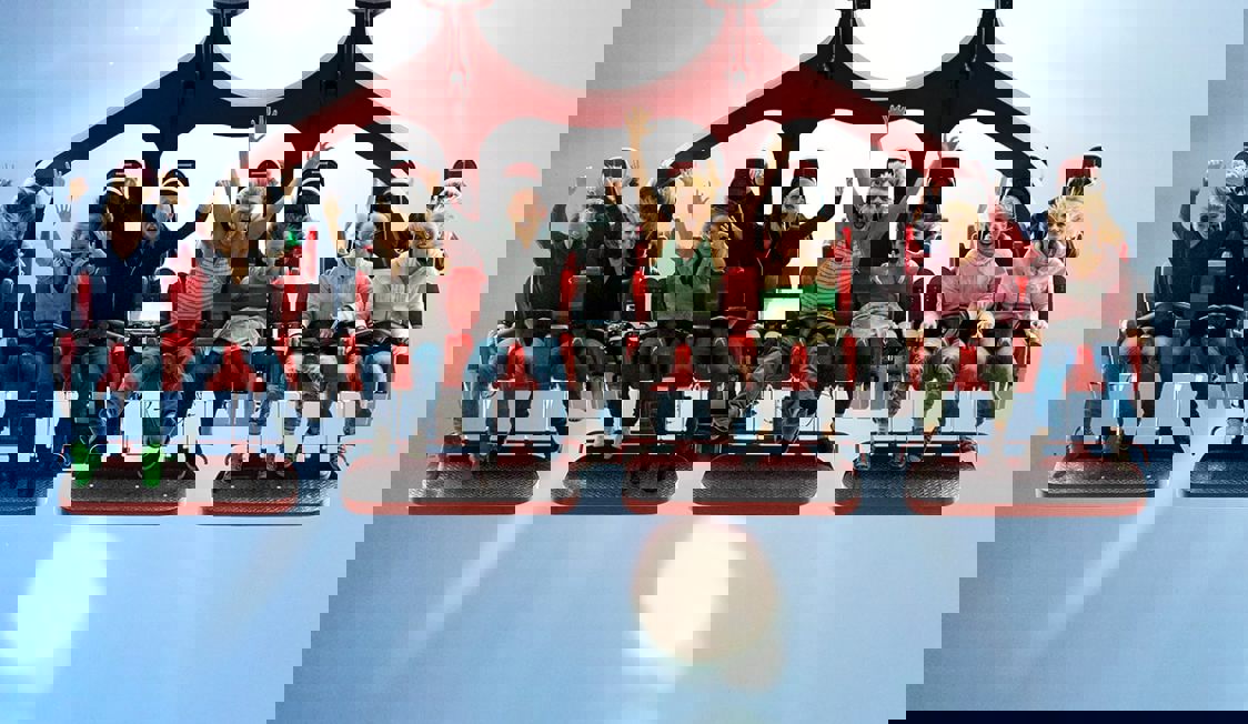 Otte børn sidder i en forlystelse og skriger med armene i vejret.