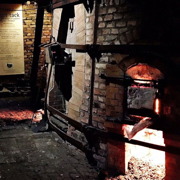 Traditionel træfyret murstensovn i funktion med ild i brændkammeret, set tæt på i en historisk bygning.