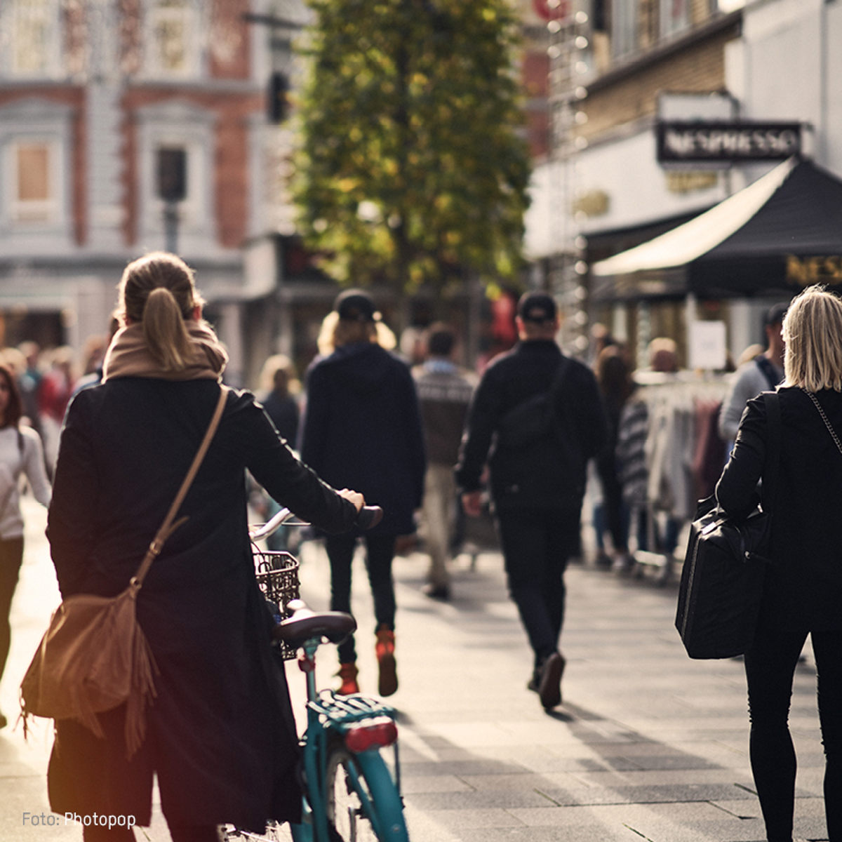 Kvinde med blå cykel går gennem travl shoppinggade i byen.