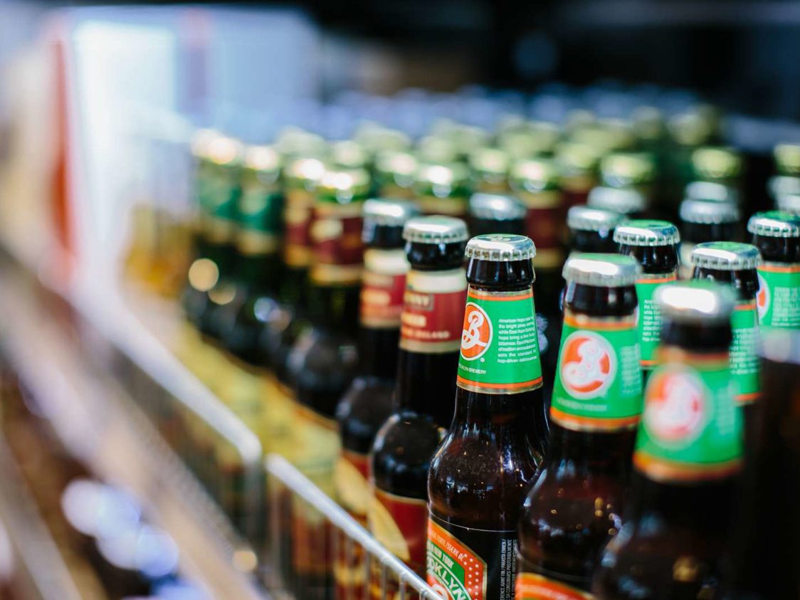Flaskor med öl uppradade på en hylla i en livsmedelsbutik med gröna och bruna etiketter i fokus.