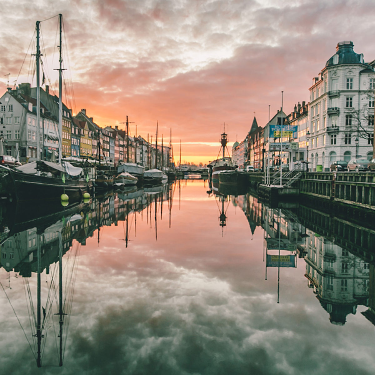 Nyhavn kanal i København med sejlskibe ved solnedgang, reflekteret i vandet.