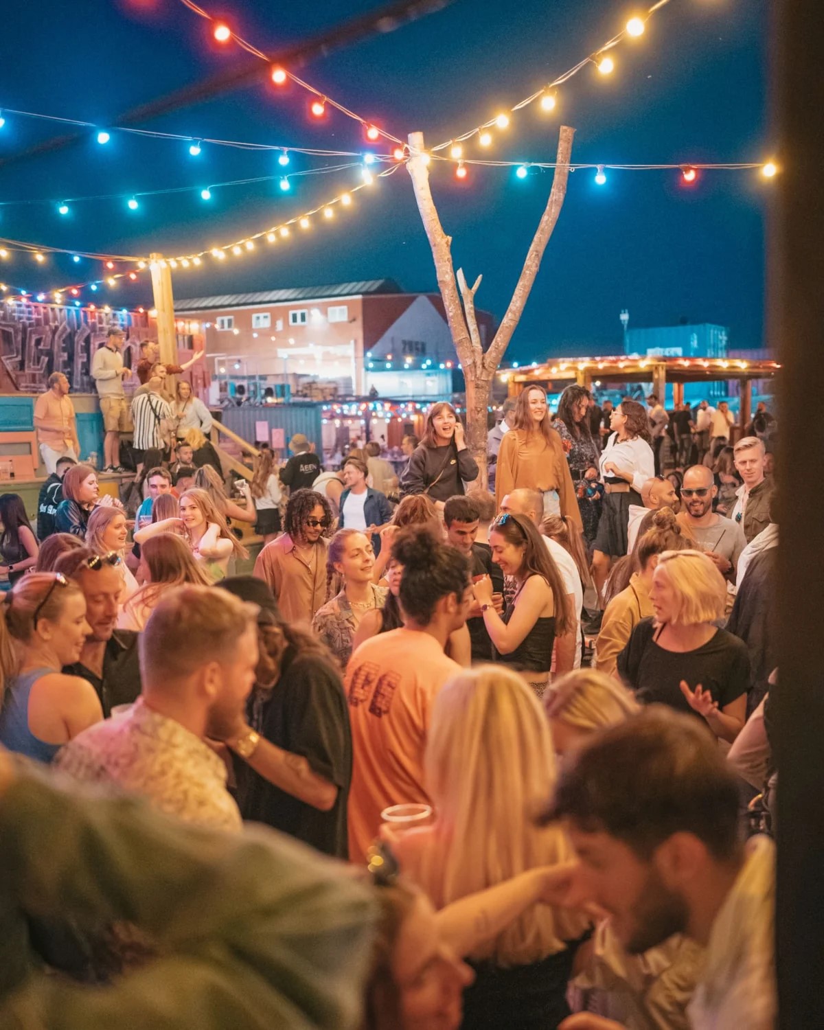 Glada människor festar på Reffen 24 under kvällen med färgglada ljusslingor och livlig atmosfär.