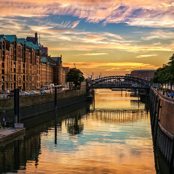 Hamnbro i solnedgången med reflektioner i vattnet och historiska byggnader längs kanalen i Hamburg.