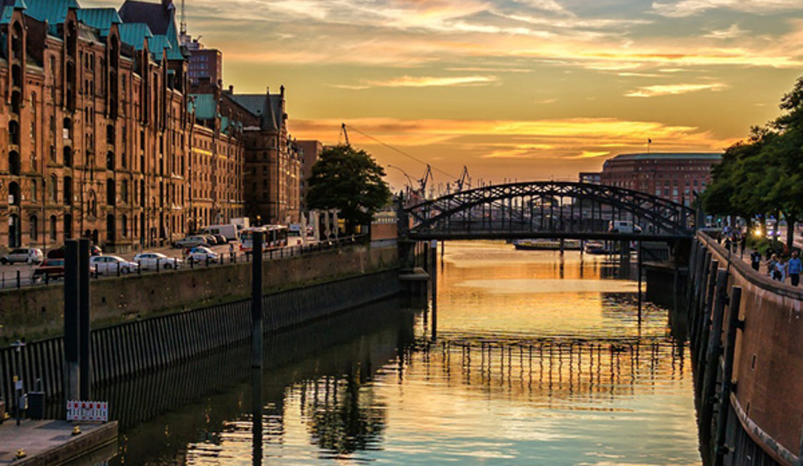 Hamnbro i solnedgången med reflektioner i vattnet och historiska byggnader längs kanalen i Hamburg.