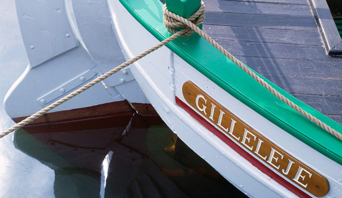 Traditionell grön och vit båt med namnet Gilleleje synligt på skylt, förtöjd vid kajen i lugnt vatten.