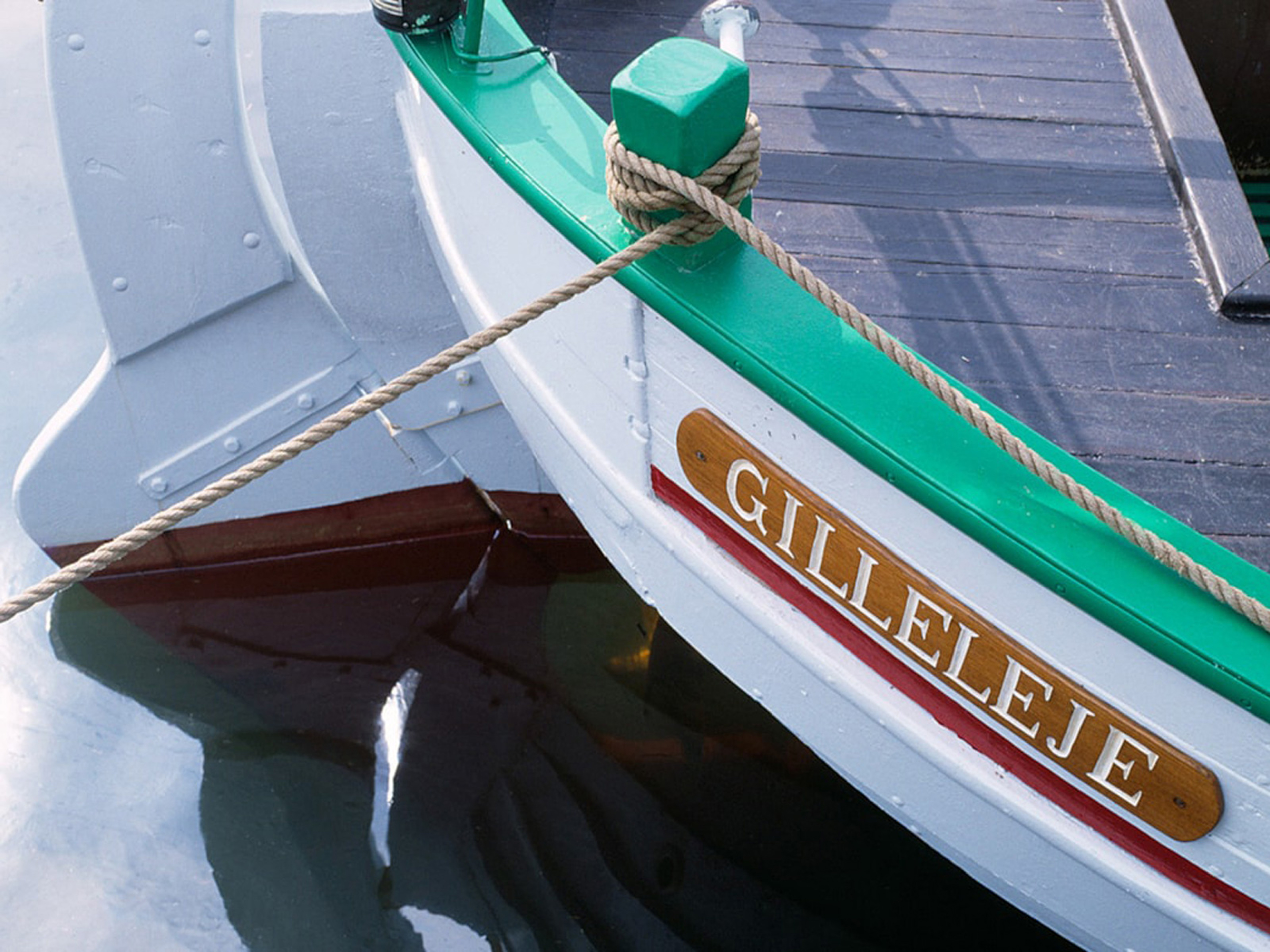 Traditionell grön och vit båt med namnet Gilleleje synligt på skylt, förtöjd vid kajen i lugnt vatten.