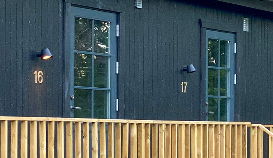 Sort træbygning med numrerede blå døre og træveranda i dagslys.