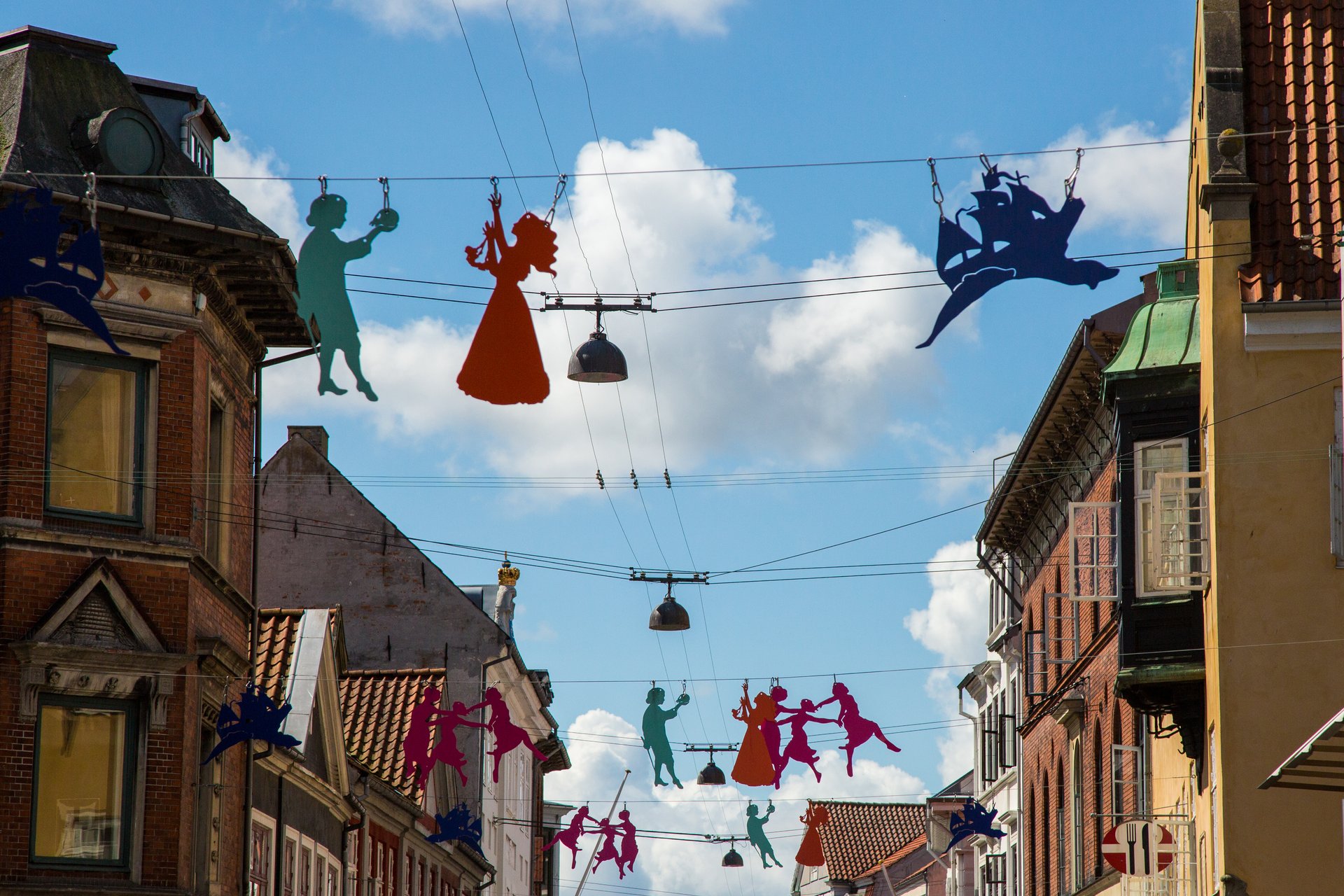 Färgglada siluetter hänger över en gata i Helsingör, Danmark, med blå sommarhimmel i bakgrunden.