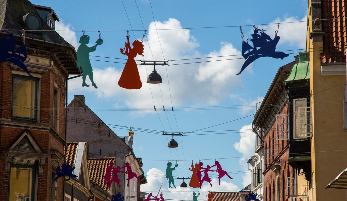 Färgglada siluetter hänger över en gata i Helsingör, Danmark, med blå sommarhimmel i bakgrunden.