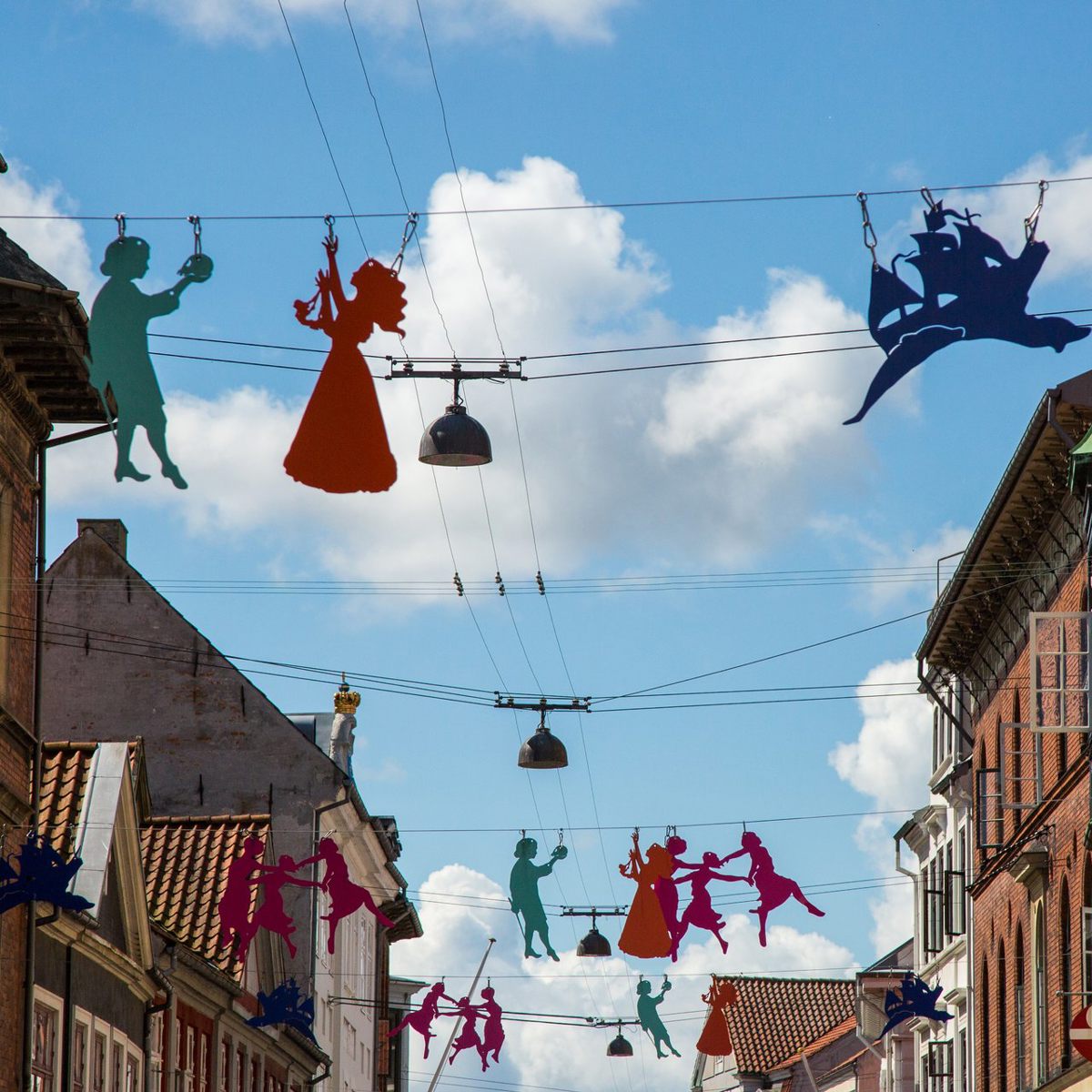 Färgglada siluetter hänger över en gata i Helsingör, Danmark, med blå sommarhimmel i bakgrunden.