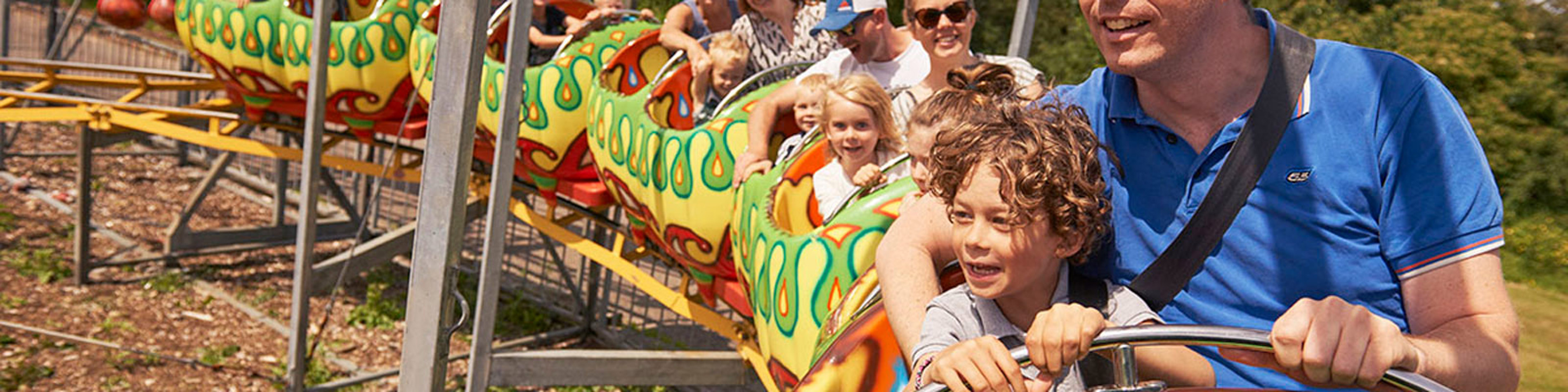 Familie nyder en tur i rutsjebanen formet som en farverig slange en solrig dag i forlystelsesparken.