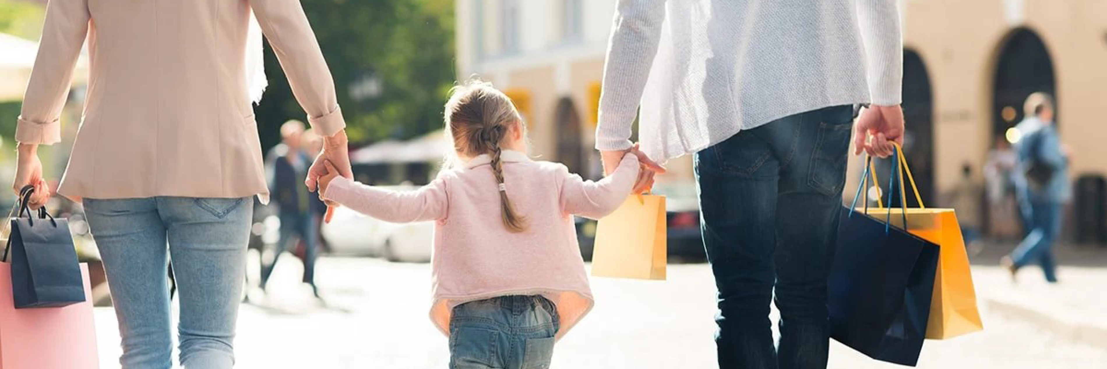 Familj med shoppingkassar promenerar hand i hand utomhus.