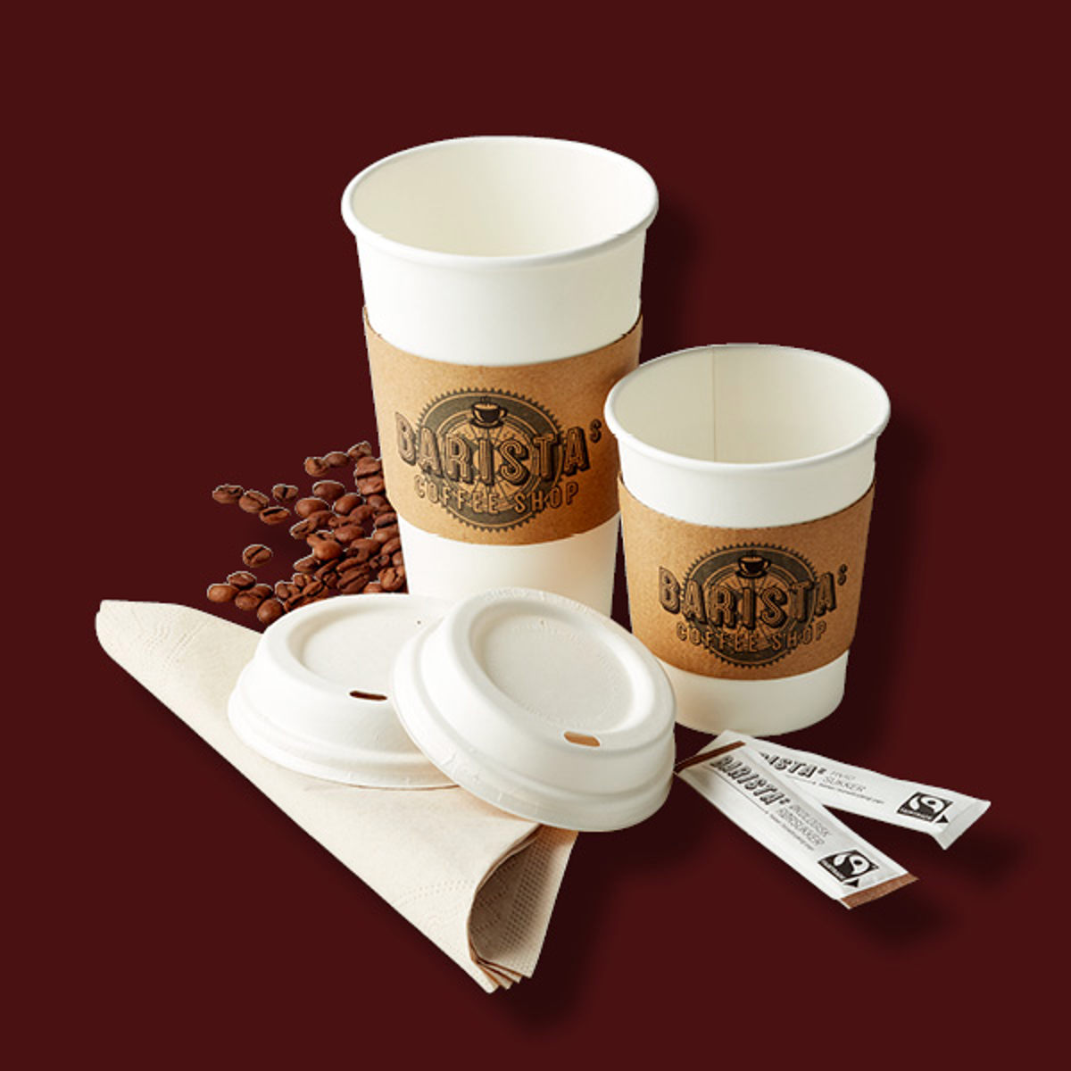 Barista kaffekopper af pap med brunt papirbånd og plastiklåg omgivet af kaffebønner og servietter.