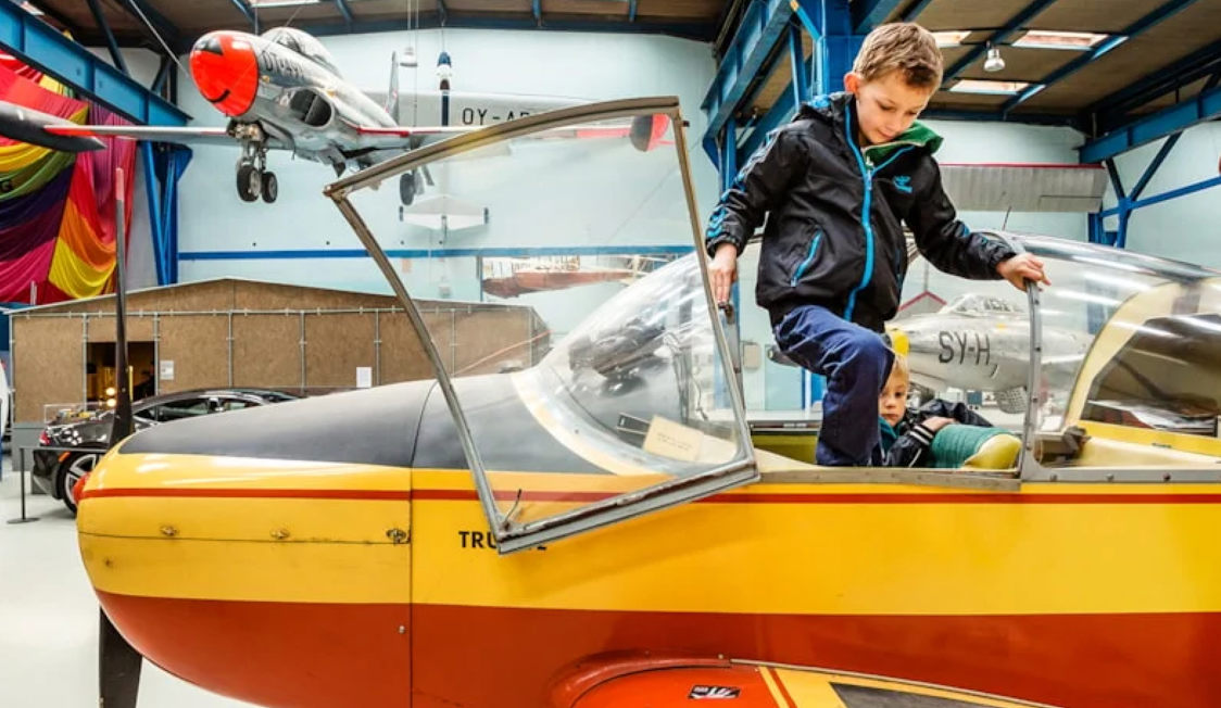 Barn klättrar in i gul och röd flygmaskinmodell Fly i flygmuseum.